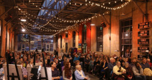 A crowd photo from a previous festival with twinkling lights hanging above them